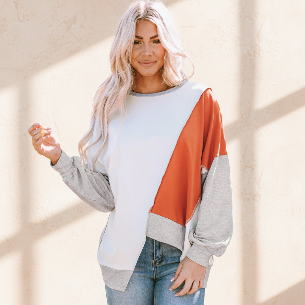 Colorblock stitching irregular hem long sleeve top on a warm ivory boutique studio background