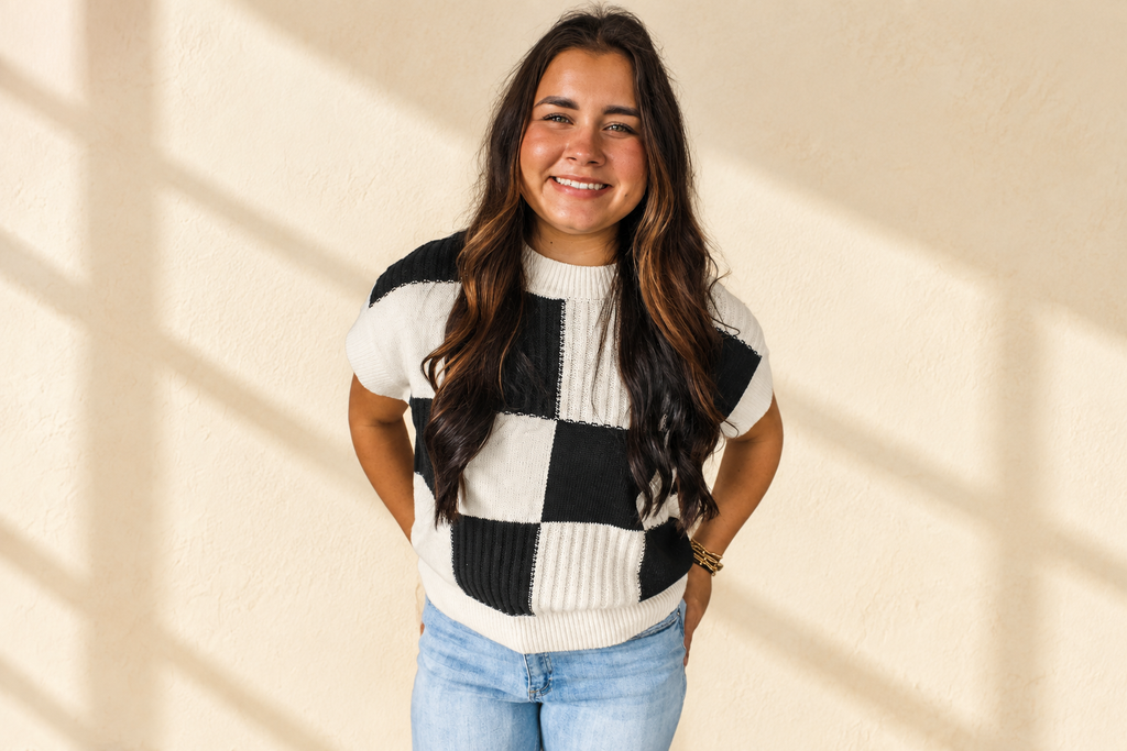 Black and white checkered color block crew neck short sleeve sweater on a warm ivory boutique background, angle 3