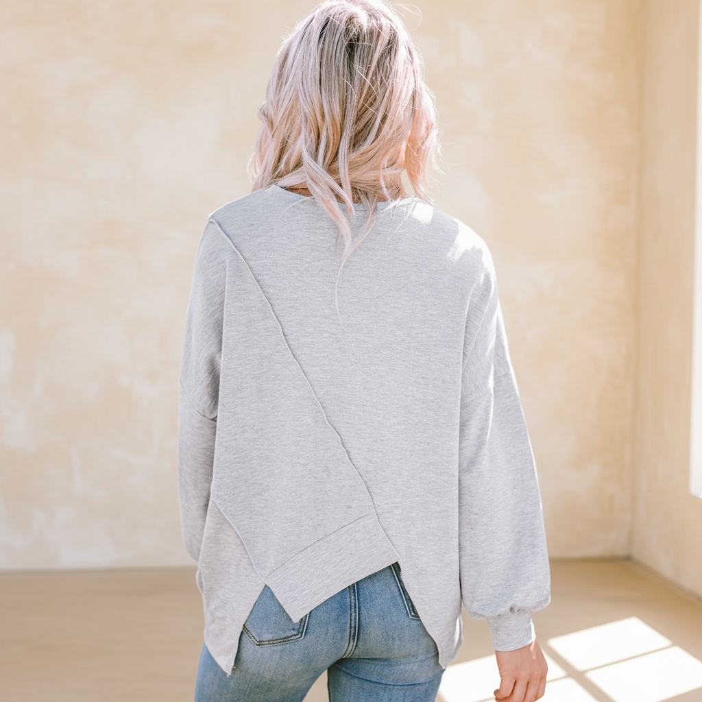 Colorblock stitching irregular hem long sleeve top on a warm ivory boutique studio background