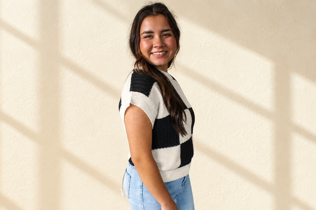 Black and white checkered color block crew neck short sleeve sweater on a warm ivory boutique background, angle 2