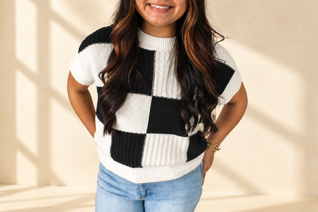 Black and white checkered color block crew neck short sleeve sweater on a warm ivory boutique background, angle 1
